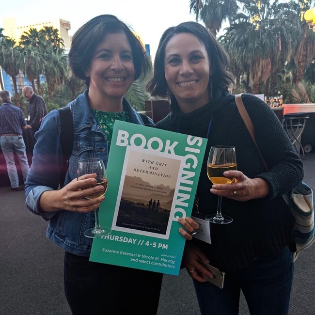 Two women holding a poster of a book cover that reads: With Grit and Determination: A Century of Change for Women in Great Basin and American Archaeology