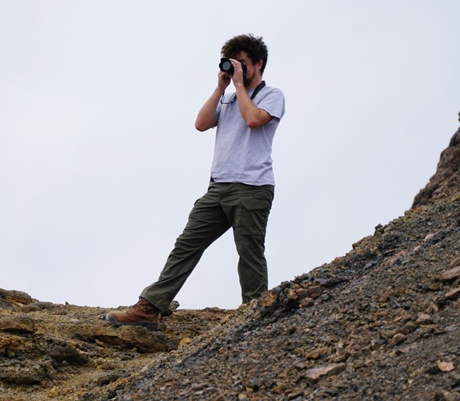 Daniel in action taking a picture Man standing on a rock looking out a camera