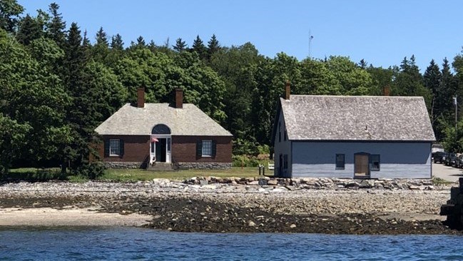 small brick building and wooden outbuilding on coast