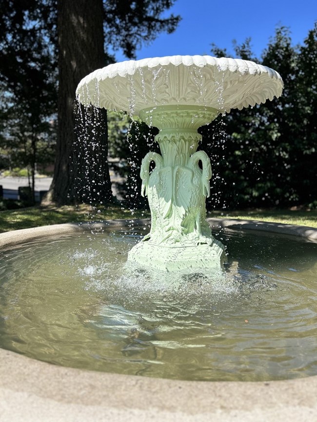 A photo of the light green and white fountain with water pouring from its basin into a pool below.