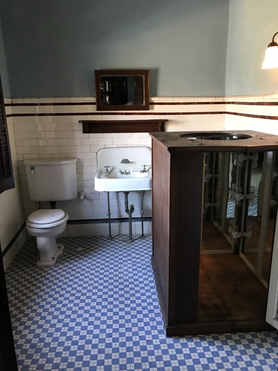 Entire view of Dr. Washington's bathroom with the original fixtures. There is a toilet, sink, mirror, a light, and a sauna.
