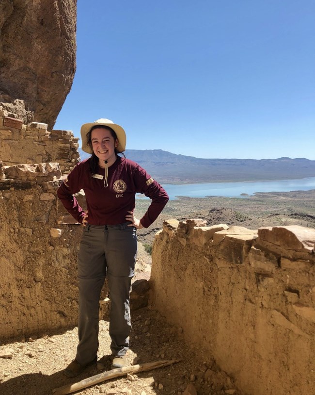 Person posing in NPS intern uniform with rock features and a lake in the background