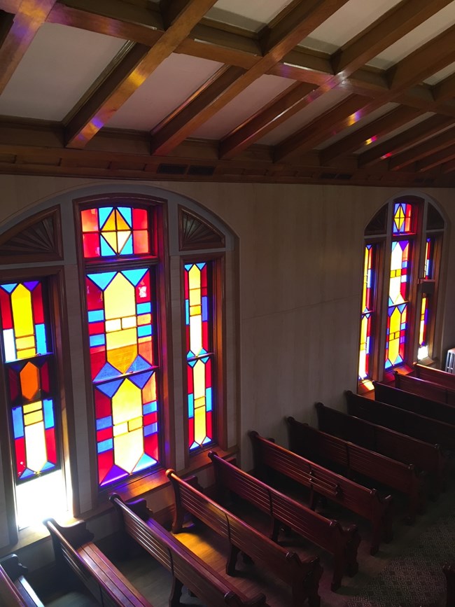 Pews in the Temple Aaron sanctuary space The pews of the sanctuary space of the synagogue against the tripartite geometric stained glass as seen from the organ loft.