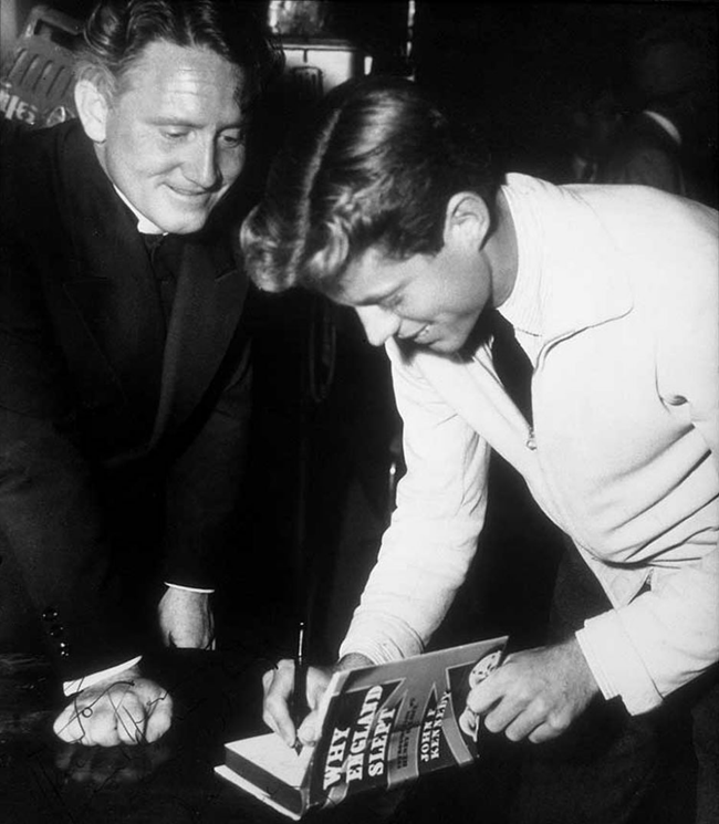 John F. Kennedy and Spencer Tracy A black and white photo of John F. Kennedy, wearing a white jacket, signing the inside the book ‘Why England Slept’ as Spencer Tracy watches in a black suit.