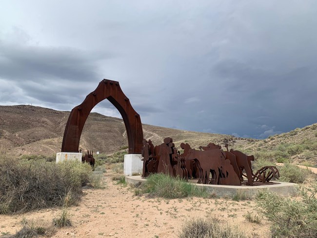 brown metal monument representing an arc and horses with people