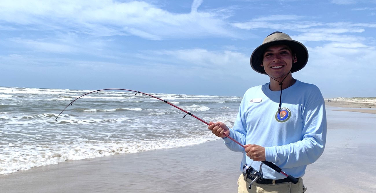 A person standing on the beach with a fishing pole