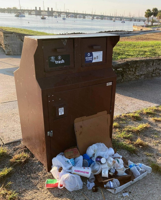 Pile of trash collects outside the trash and recycle bins.