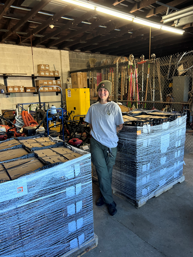 A woman in a garage smiling in front of two big piles of boxes.