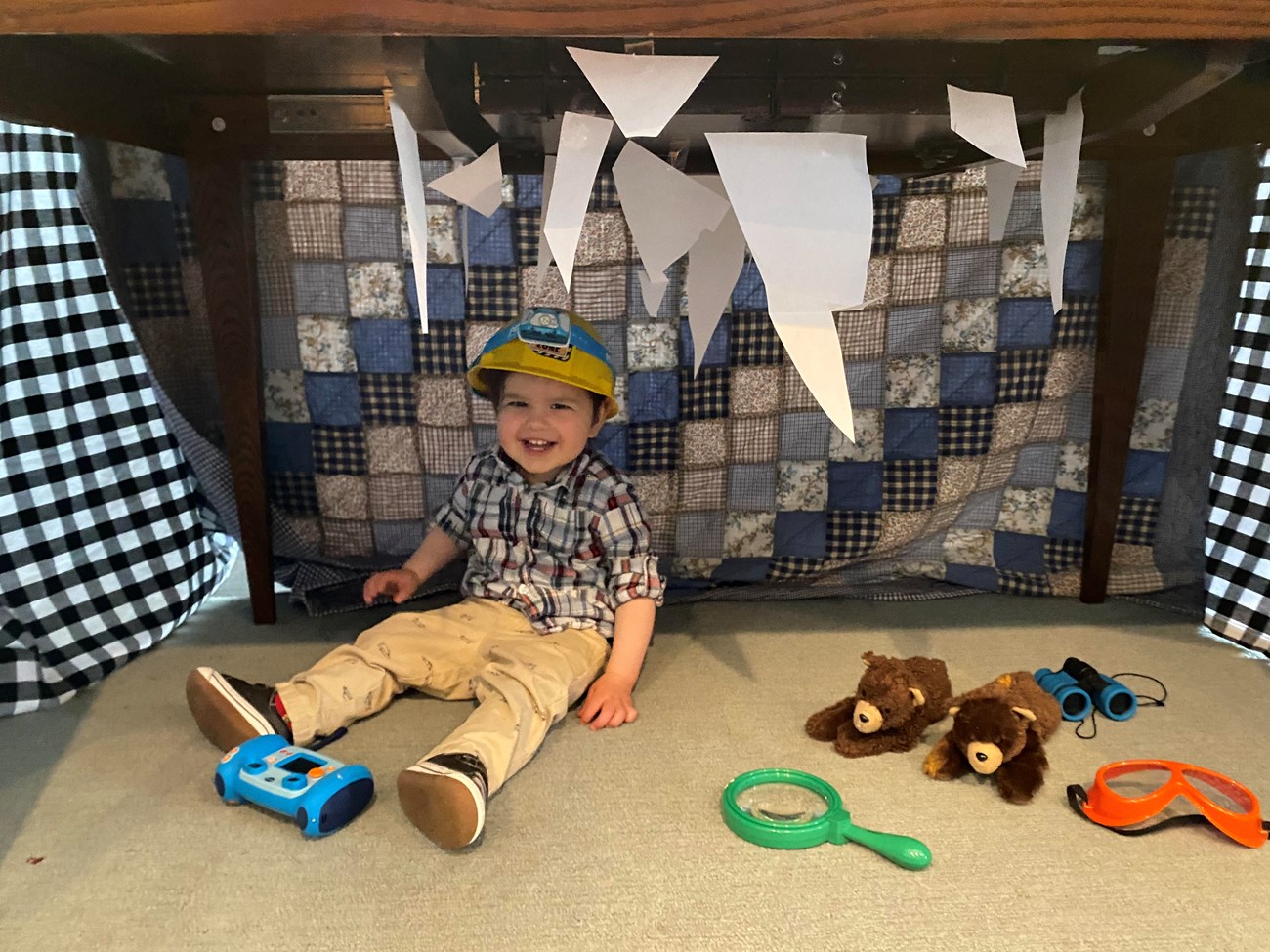 child in a homemade cave fashioned out of a table and blankets