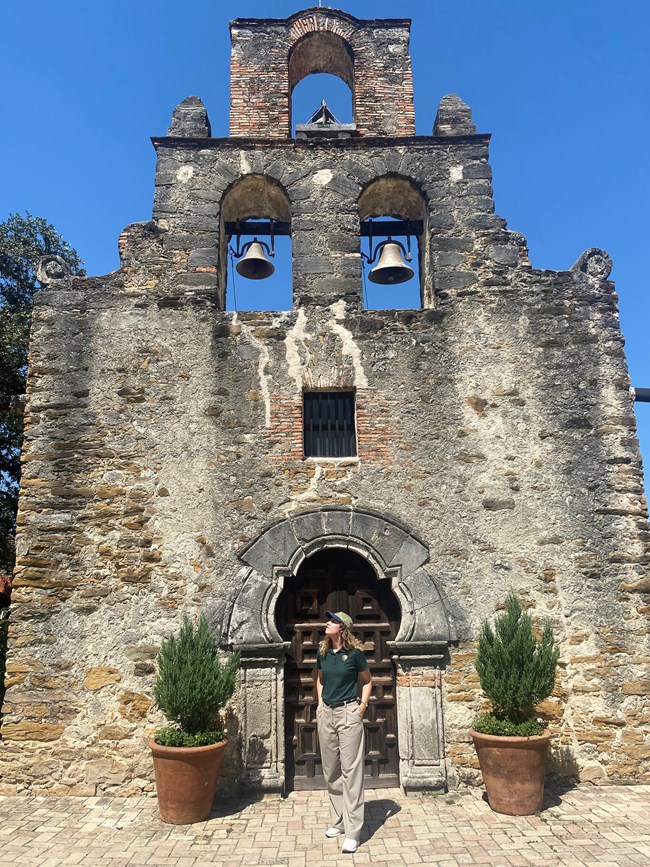 Woman standing in front of stone church with three bell towers