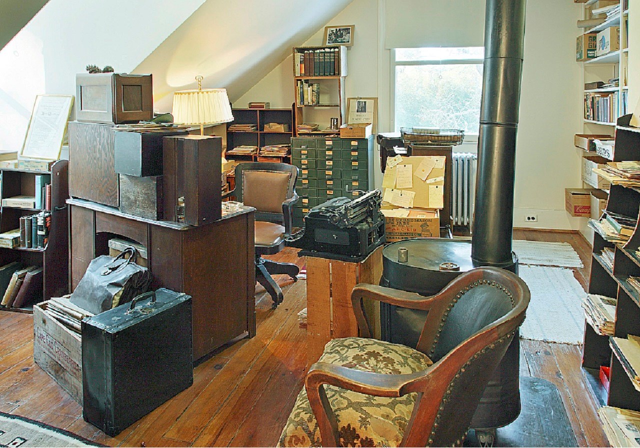 A loft office filled with books, metal file cabinets, office desk and chair, and a wood stove.