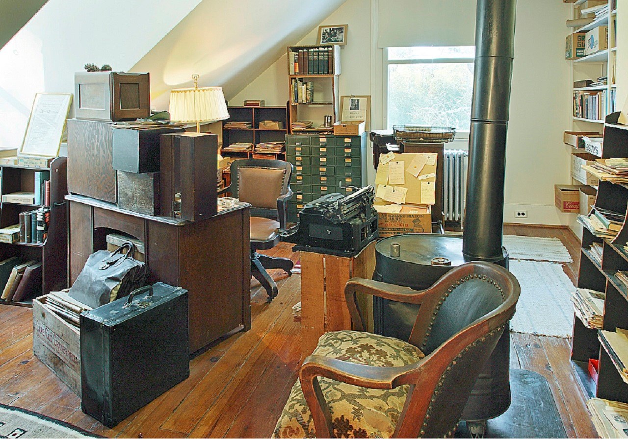 upstairs study A loft office filled with books, metal file cabinets, office desk and chair, and a wood stove.