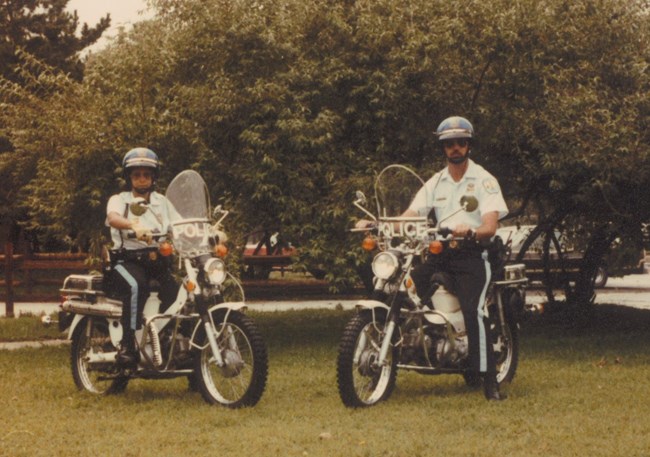Two US Park Police officers sitting on police motorcycle scooters.