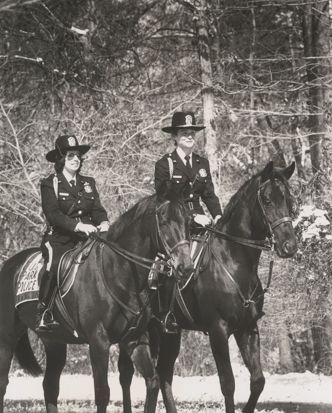 Two women in Park Police uniforms ride horses.