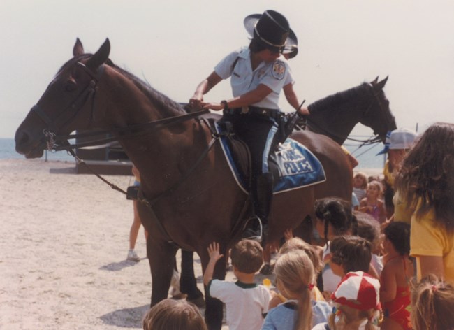 Officer Valerie Fernandes sitting on a horse with children around them.
