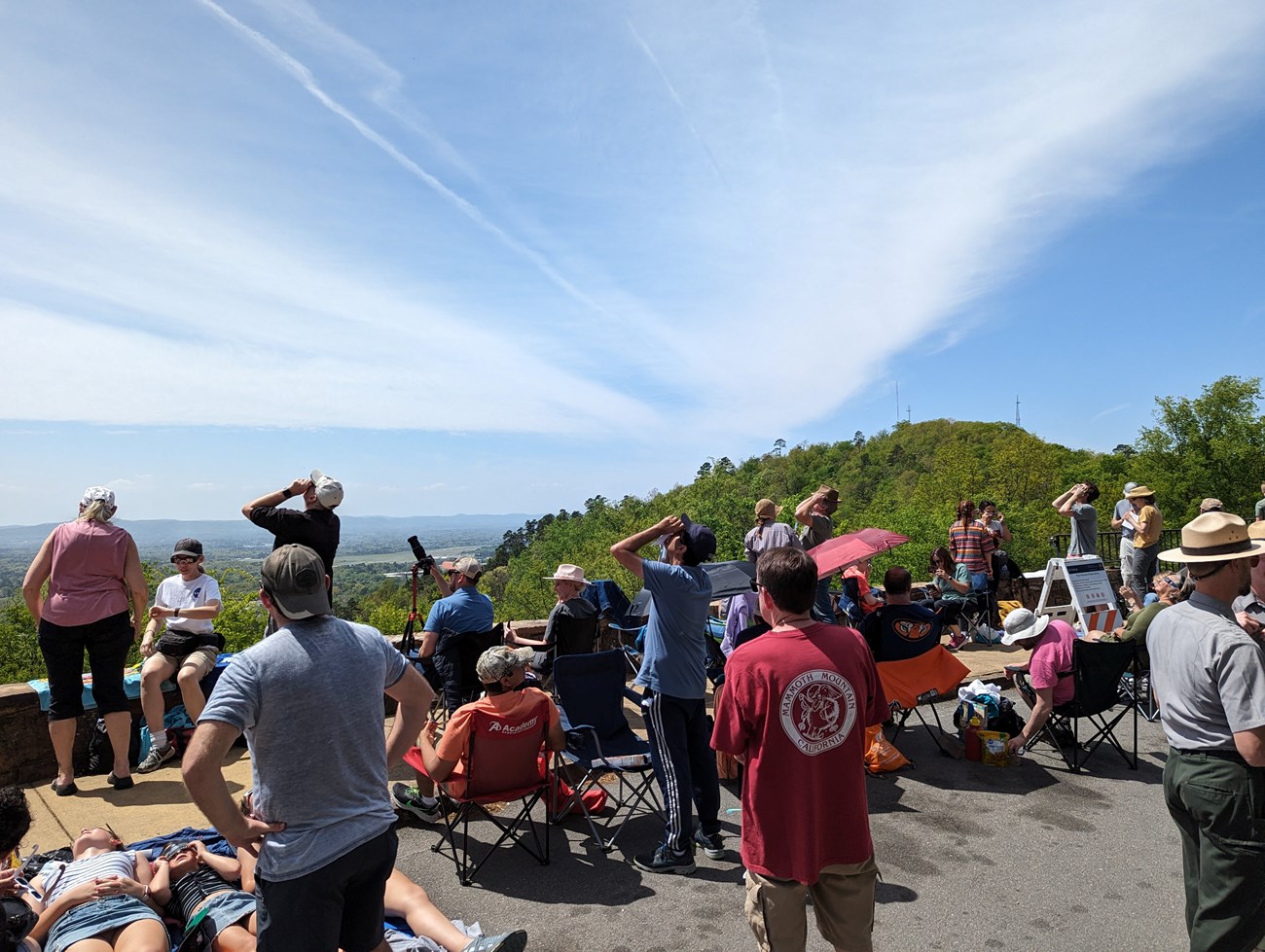 Viewing comfort options on West Mountain_JulieHoover NASA Group of people gather at a park overlook and look up at the sun with protective viewers. Forrested hilltop in background. Park Ranger in foreground.