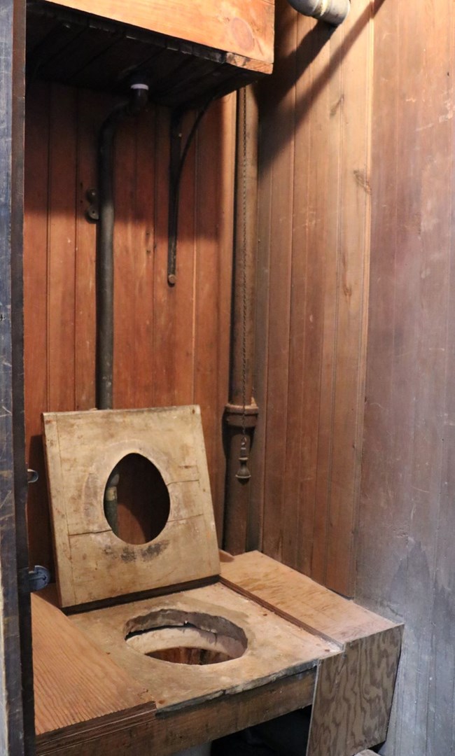 water closet Toilet with a wooden seat and a high wooden tank with pull chain