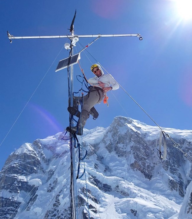 A researcher climbs a weather station tower to install.