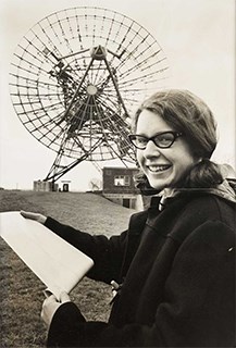 web Jocelyn Bell Burnell National Media Museum Science & Society Picture Library Woman holds a piece of paper in front of a large metal satellite dish