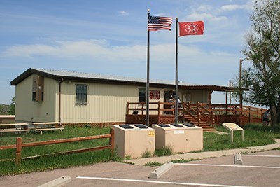 american and lakota flags fly on the porch of a small white building