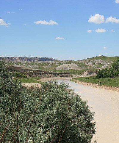The white river meandering through the fields with badlands formations in the background