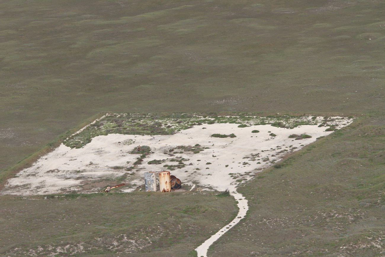 an aerial view of an old well pad with rectangular bare patch of ground with rusty equipment