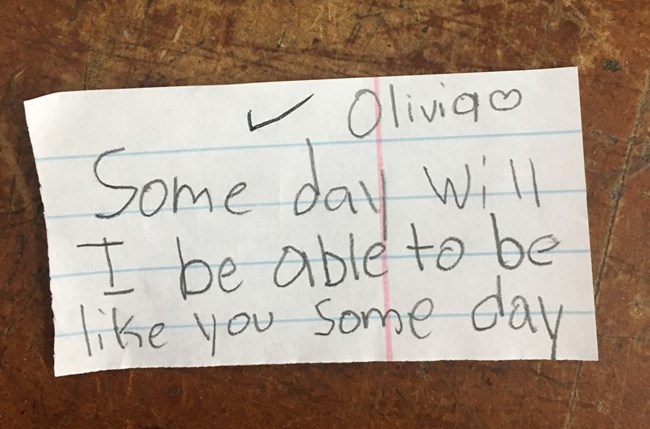 A slip of lined paper contains a handwritten question from a 4th-grade student reading “Olivia - some day will I be able to be like you some day”
