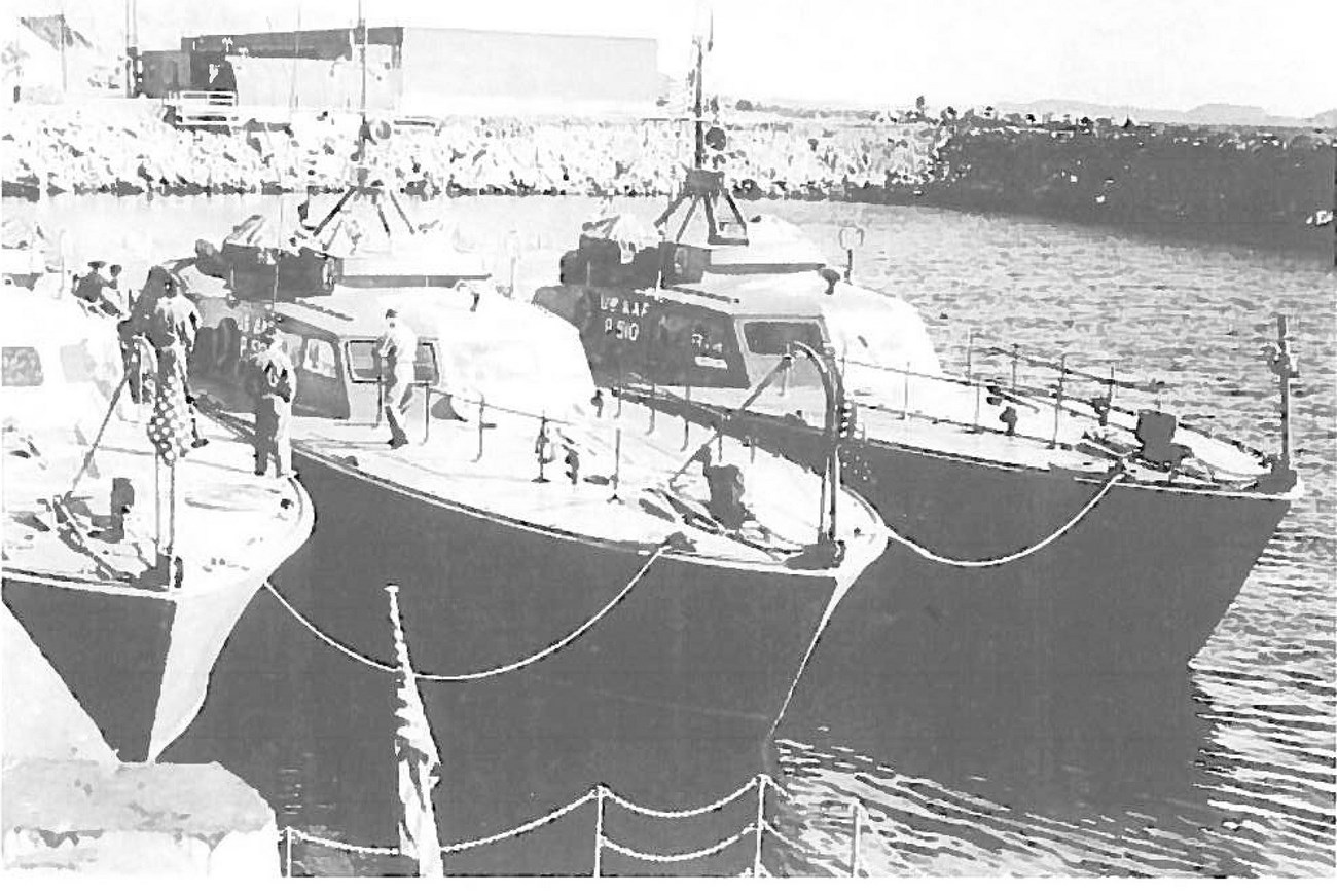 Black and white photo of three boats side by side at dock, with a few people on deck.