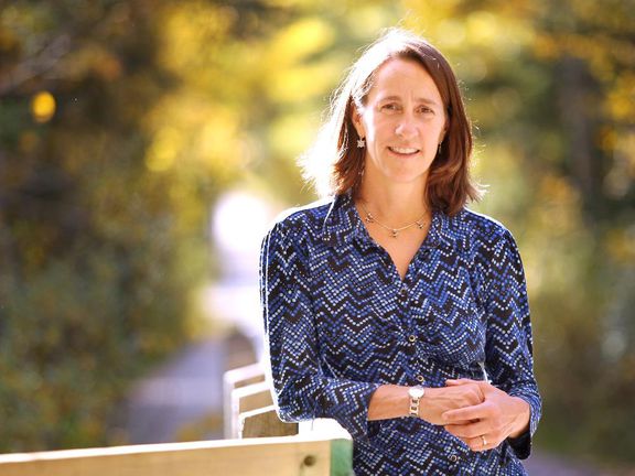 Jodi Hilty woman leans against bridge railing with a forest in the background as she looks at camera