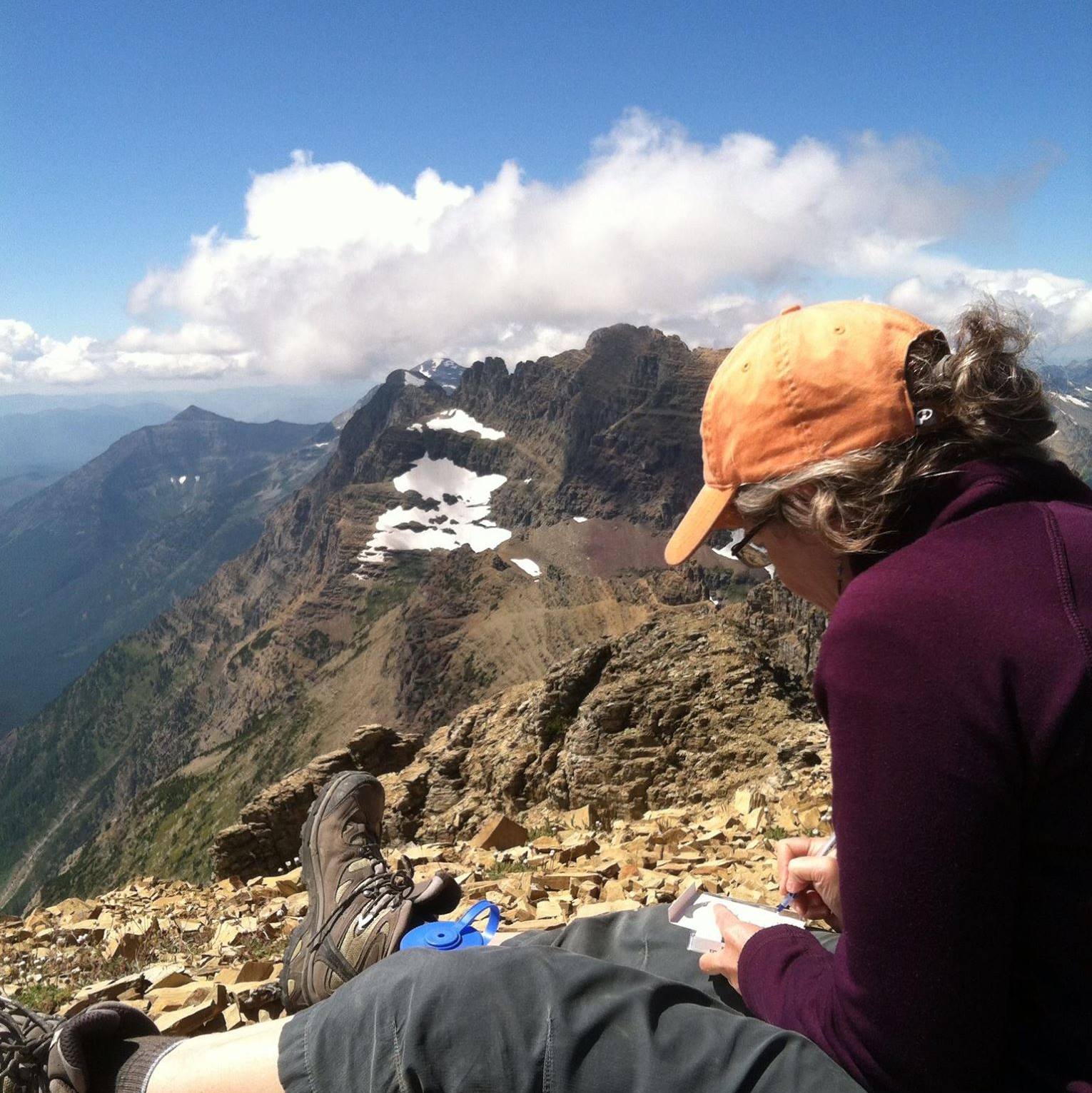 Mary Riddle women writes in field book at the top of a mountain