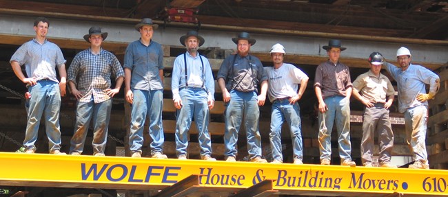 A group of men stand in a row. They are dressed for physical labor.