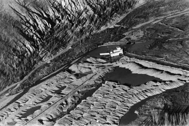An aerial black and white old photo of a dredge mining operation along the Yukon River.