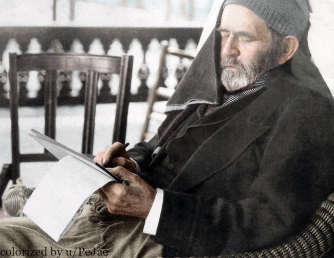 Grant seated in a chair wearing a cap and coat and writing on a notepad.