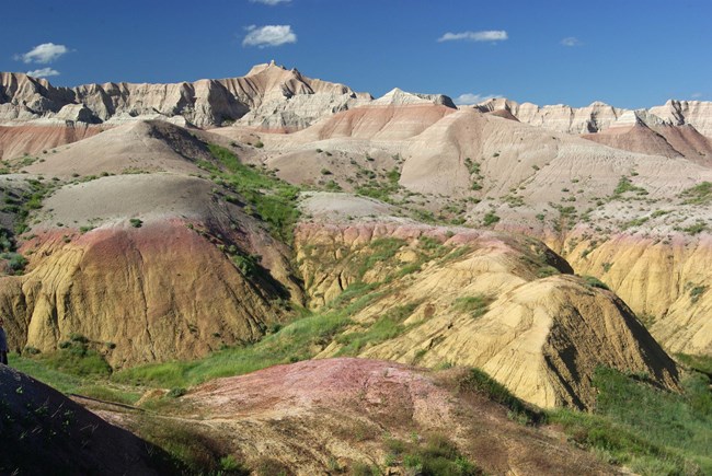 brightly colored yellow, red, and brown layers of badlands formations. a red layer appears both at the top of a peak and in a low valley, just feet away.