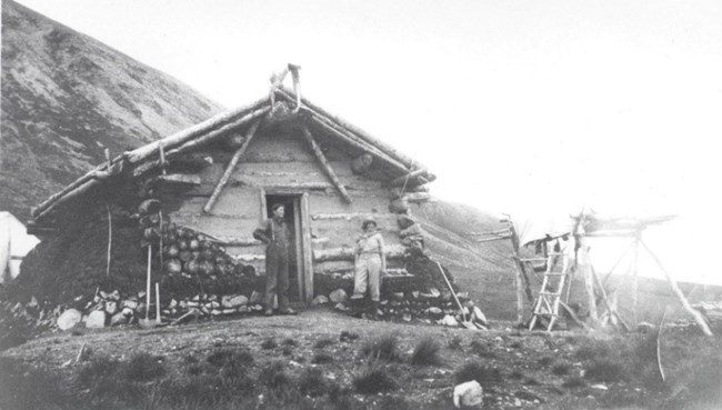 two people standing outside a rustic log cabin