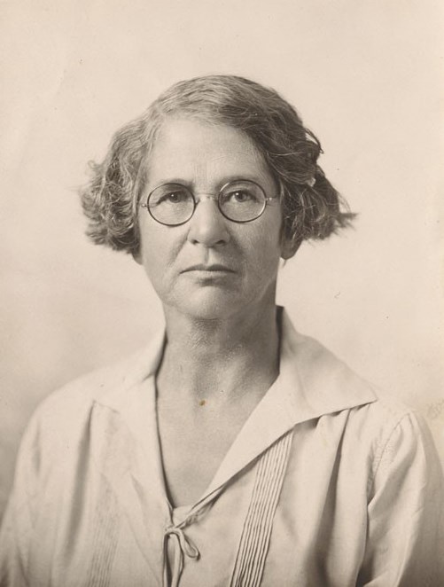 sepia toned portrait style photo of a woman with glasses, a short haircut, and a white blouse