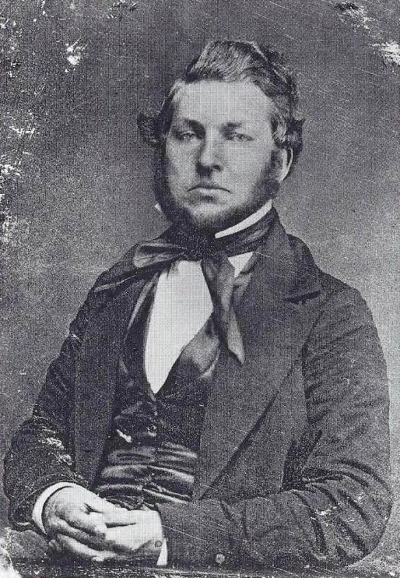 young man with wavy brown hair wearing a tattered suit jacket and tie that is twisted