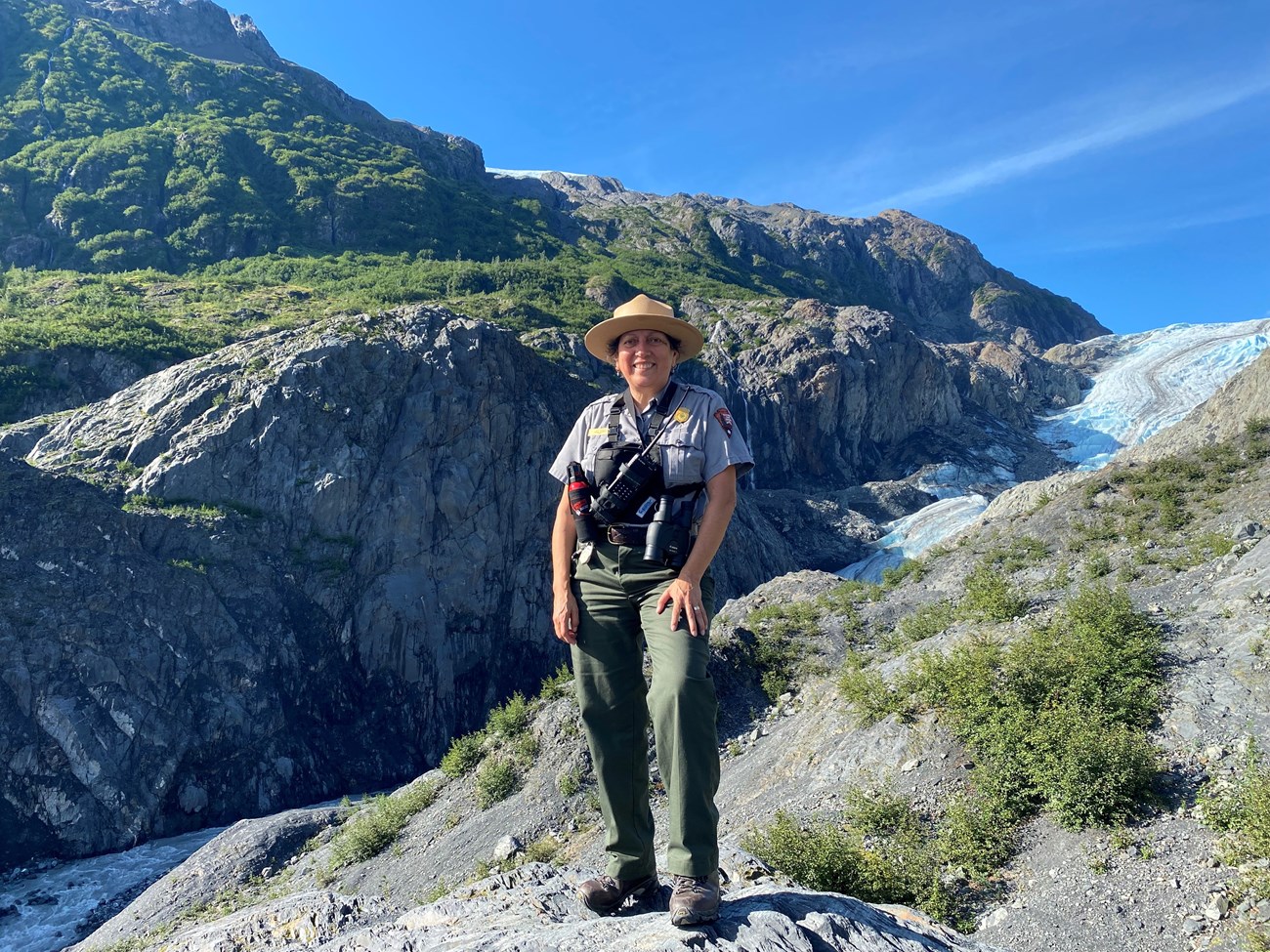 Yuri Blano at Kenai Fjords National Park. A ranger on a rocky terrain with a glacier coming down a valley.