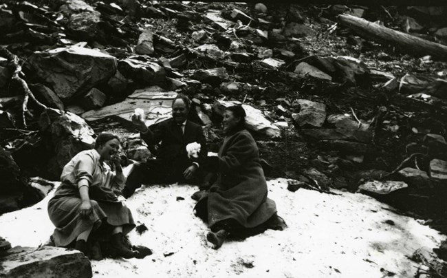 black and white photo of two women and a man sitting on snow and laughing