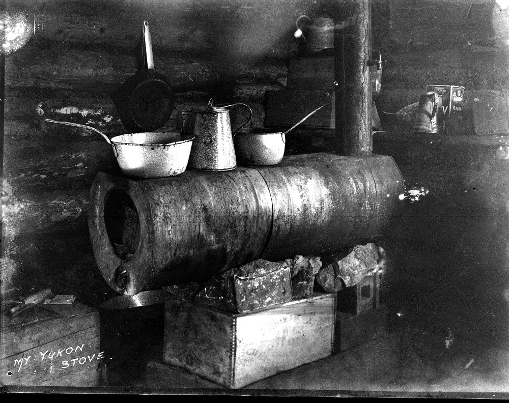 A makeshift kitchen with cooking pots and a coffee pot sitting on a stovepipe stove.