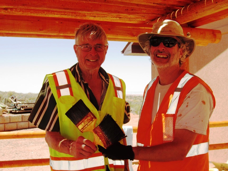 two smiling men in safety vests holding paint brushes
