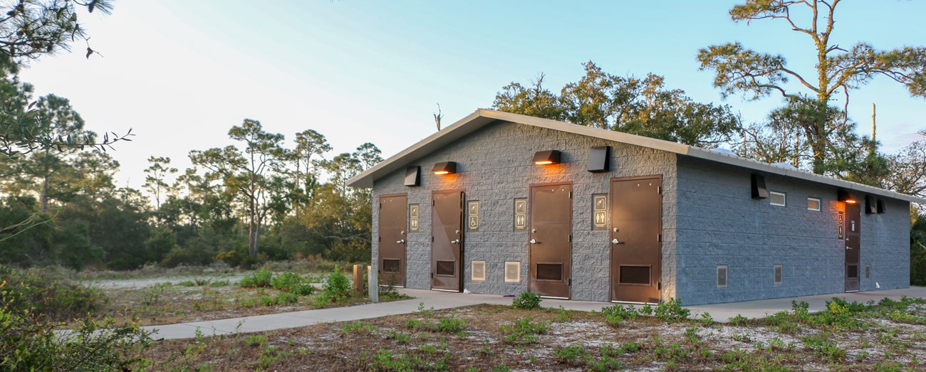 A restroom building stands among trees at sunset A restroom building stands among trees at sunset