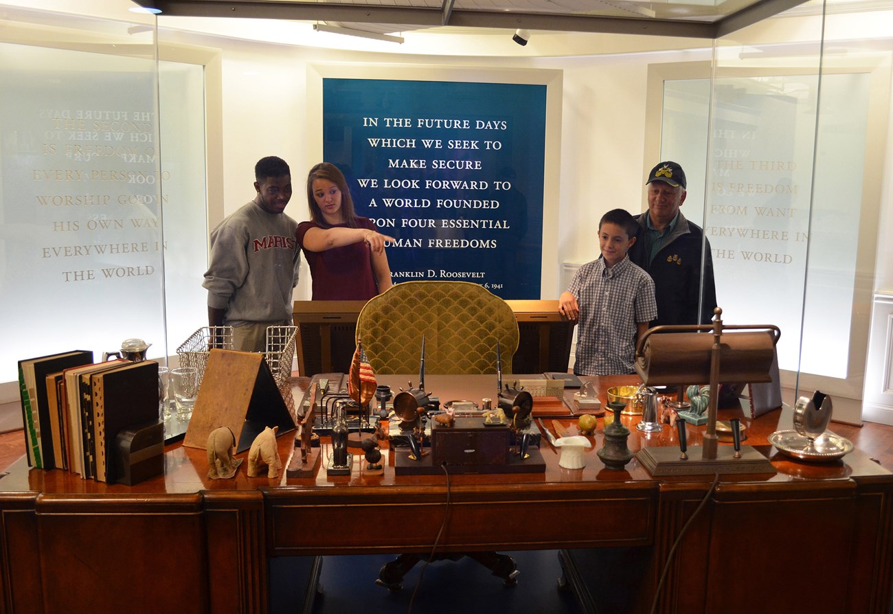 Four people looking over a cluttered desk.