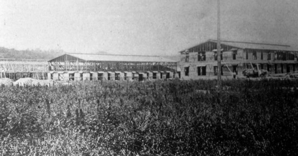 Two-story buildings under construction Several wooden buildings being constructed in front of a grassy field