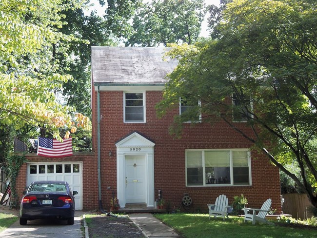 View of a two story red brick house with a tree in front