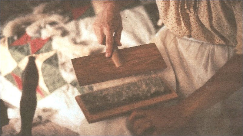 Someone brushing wool between two comb-like objects. National Park Service. Someone brushing wool between two comb-like objects. National Park Service.