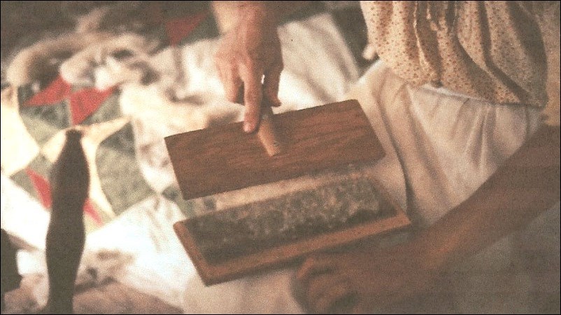 Someone brushing wool between two comb-like objects. National Park Service.