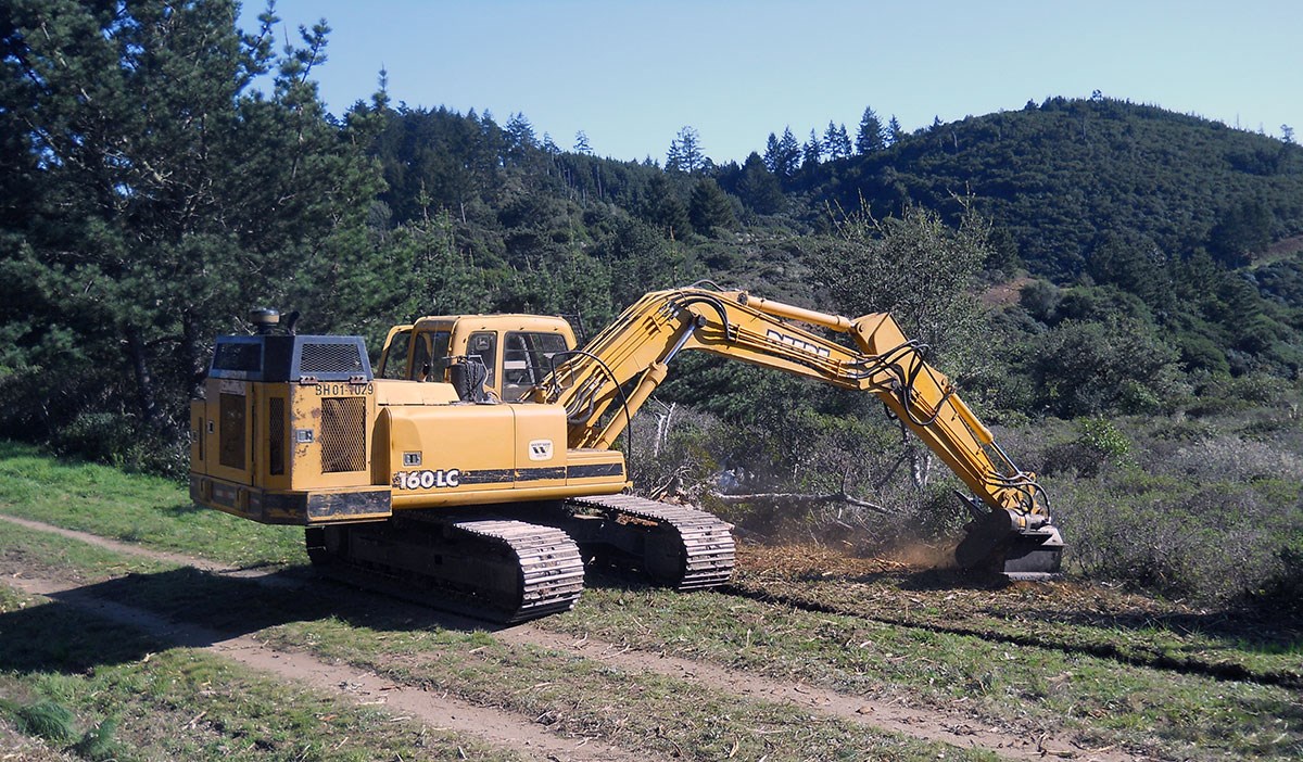 An excavator digs off the side of a dirt road/trail