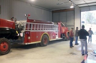 People stand in and near an engine bay with a fire truck.