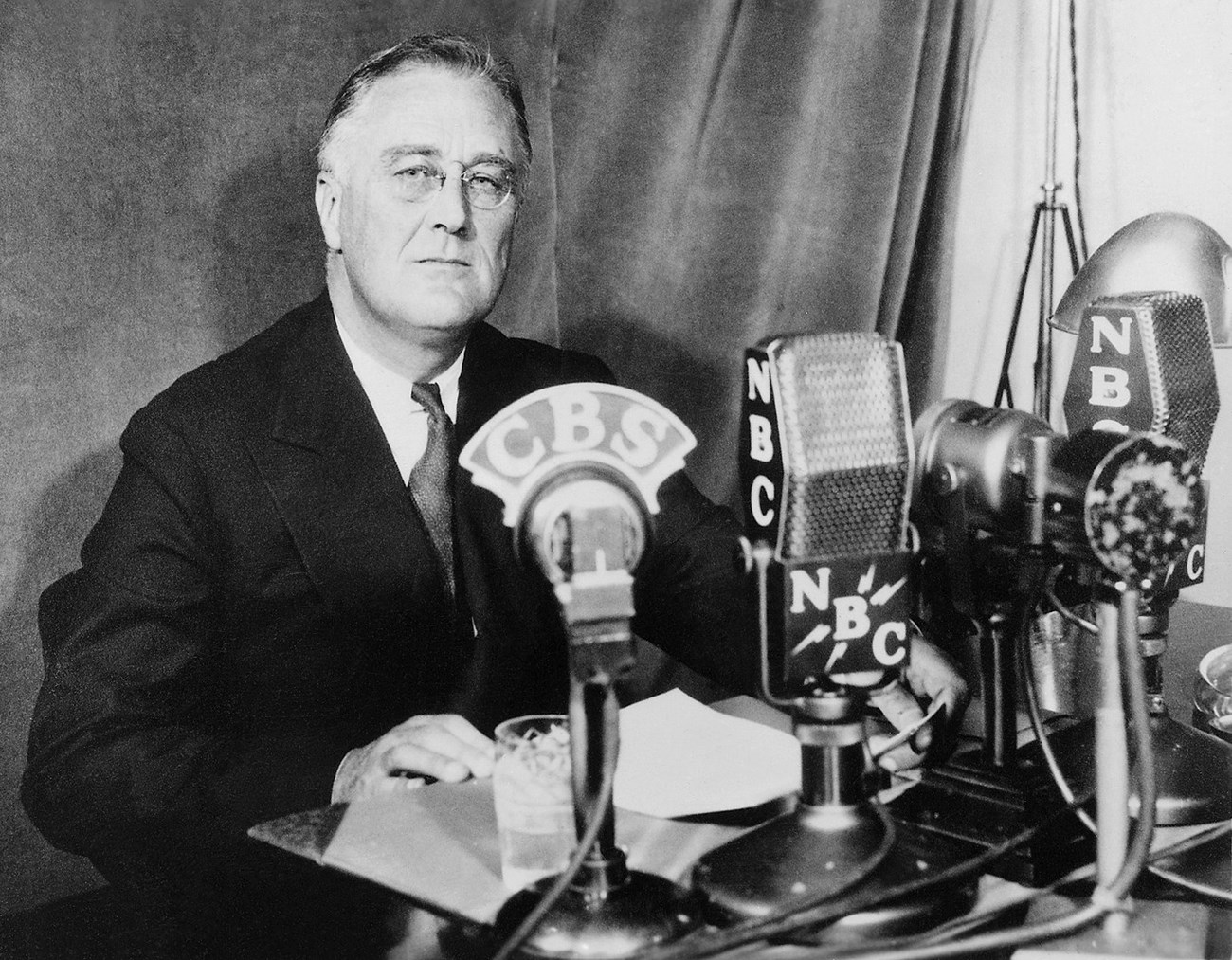 A black and white image of a man at a desk delivering a radio address.